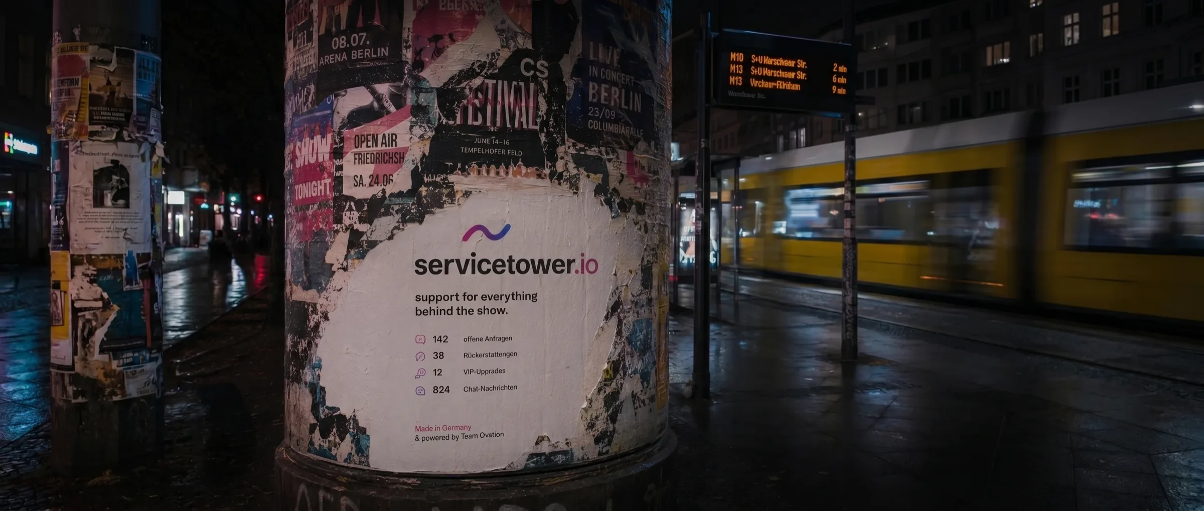 servicetower.io Plakat auf einer Berliner Litfaßsäule bei Nacht, daneben eine Tram an der Haltestelle Warschauer Straße